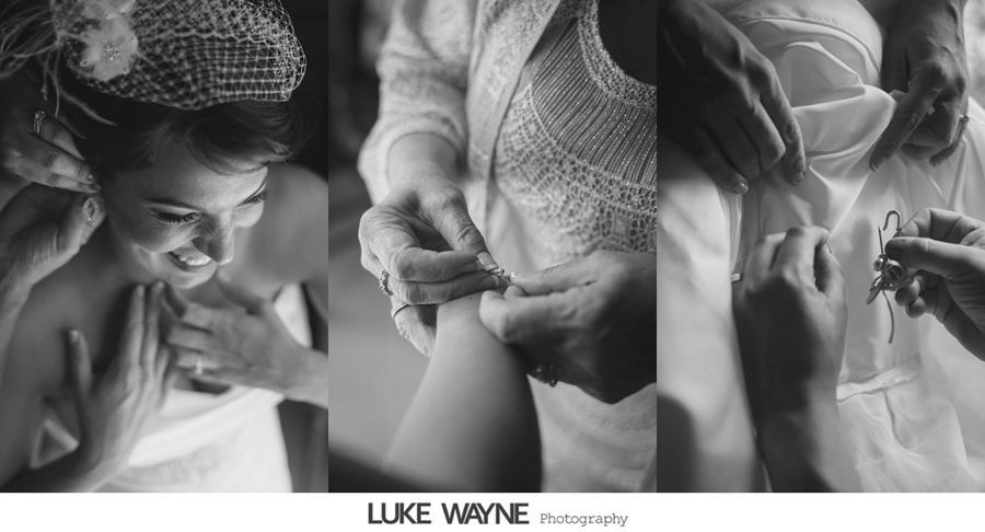 Bride getting dressed, assisted by two people, attaching buttons on the dress in a candid moment. Black and white.