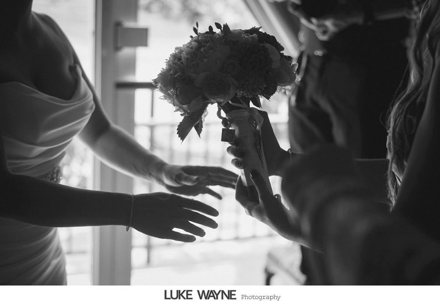 Bride receiving bouquet, with hands reaching. Black and white photo near window.