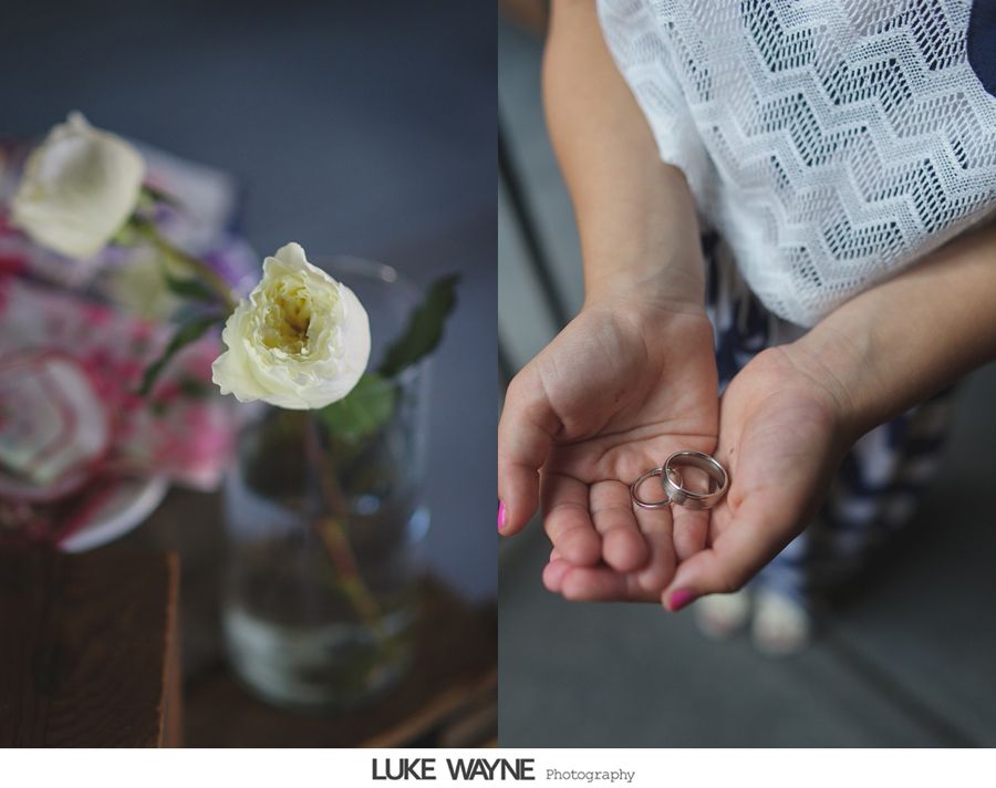 White rose in glass vase next to woman holding wedding rings in hands.