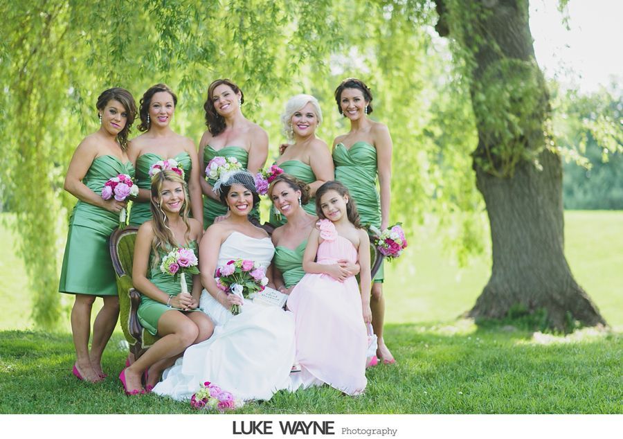 Bridesmaids in green dresses with bride in white dress, pose outdoors with a girl in pink.