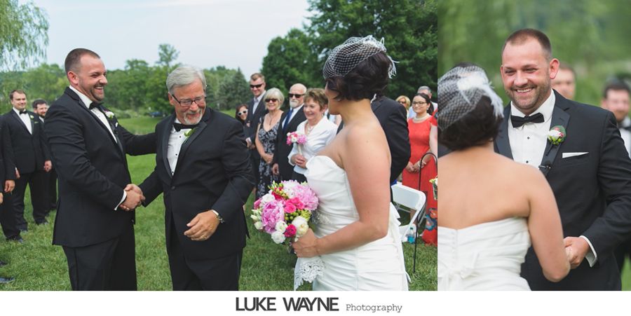 Groom shakes hands with the bride's father at an outdoor wedding ceremony. Bride smiles, holding a bouquet. Guests watch.