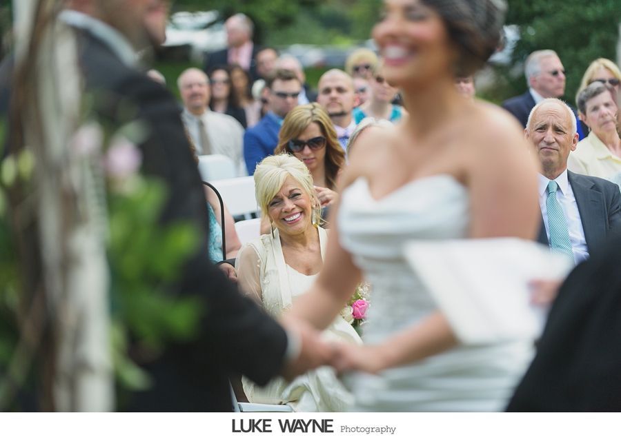 Wedding ceremony: Bride and groom holding hands, smiling; guests watch.
