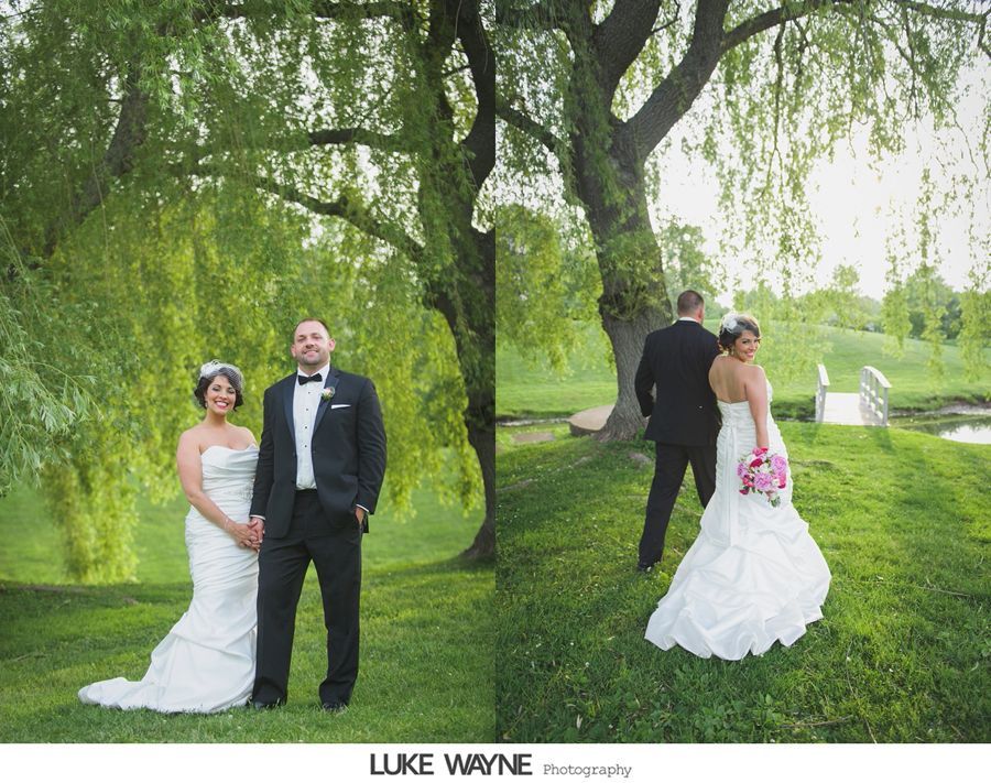 Wedding couple under willow tree; bride and groom stand holding hands, poses for photos outdoors.