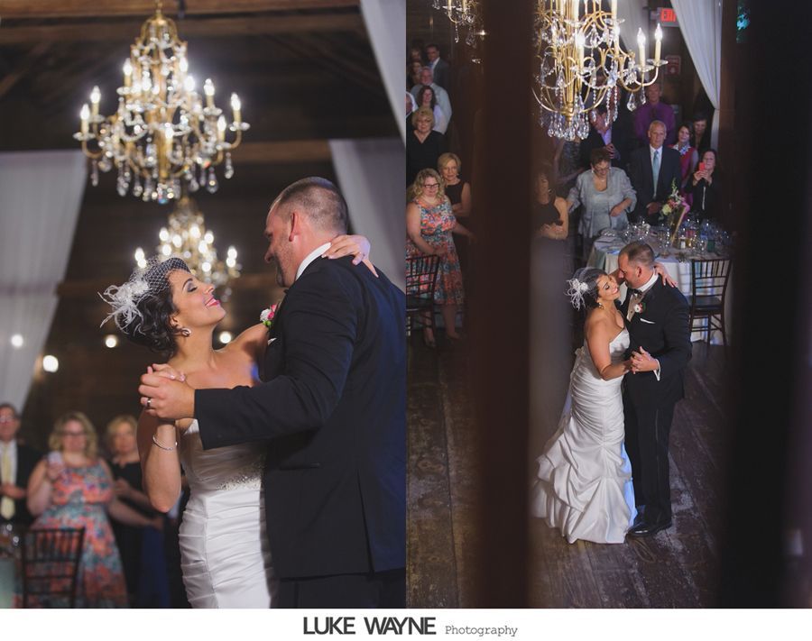 Wedding couple dancing in a decorated venue with chandeliers and guests. They are embracing, smiling.