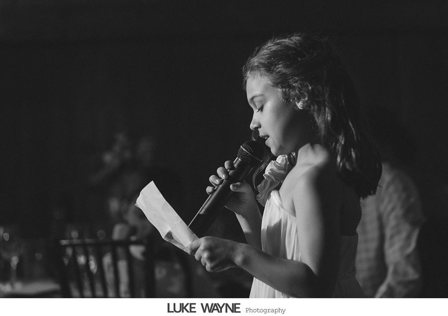 Girl holding microphone, reading from papers, lit from the side at event, black and white.