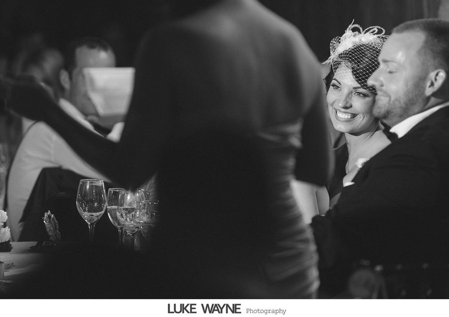 Bride and groom at a wedding, smiling during a toast. Black and white.