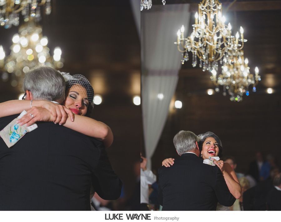 Bride and father embrace on the dance floor under a chandelier at a wedding reception.