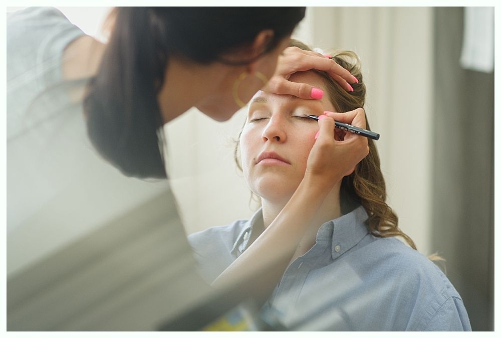 Makeup artist applying eyeliner to a person's closed eye in a well-lit room.