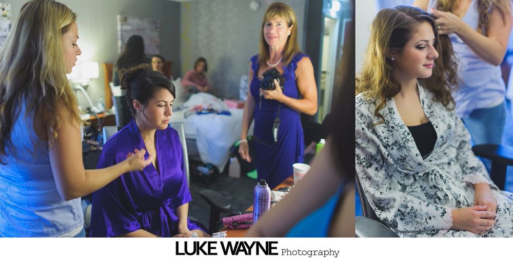Woman having makeup applied, reflected in mirror. Person in teal robe applies makeup to woman in gray robe.