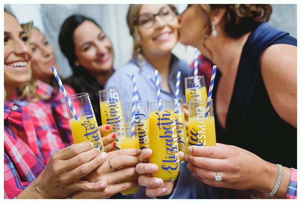 Bridesmaids toasting with champagne flutes; one gets kissed. Drinks have blue straws & names.