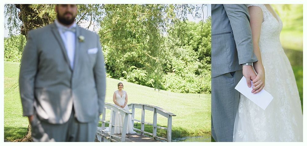 Groom in suit looks at bride on bridge. Other groom holds bride's hand, holding a card. Wedding scene.