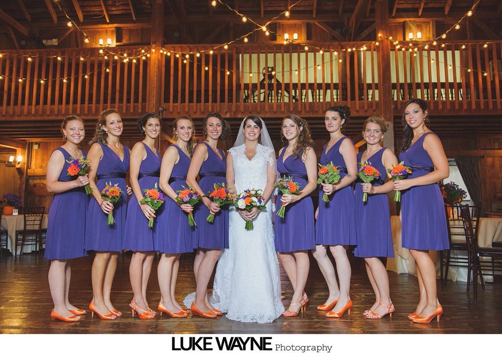 Bride smiles surrounded by teal-clad bridesmaids, holding bouquets in an orchard.