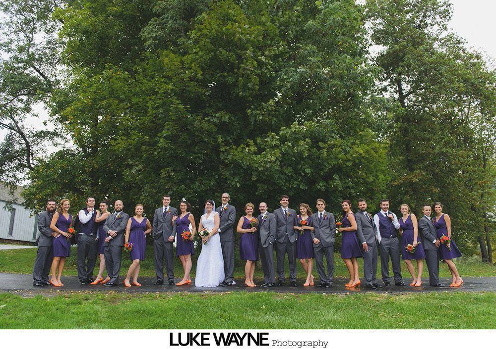 Groom and groomsmen in black suits and sunglasses pose in front of a colorful autumn landscape.