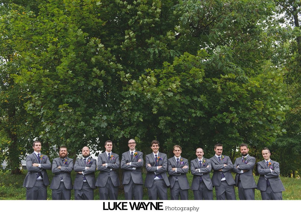 Bride with bridesmaids in teal dresses, posing outdoors. Some bridesmaids have playful expressions.