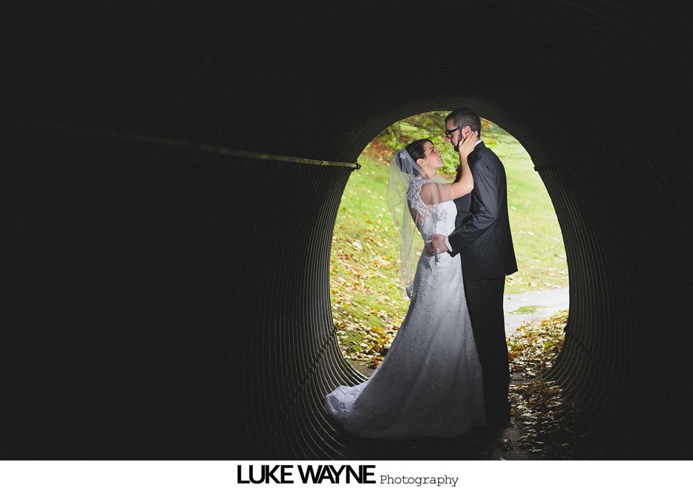 Bride in a strapless gown stands in an orchard, holding a bouquet. Black and white.