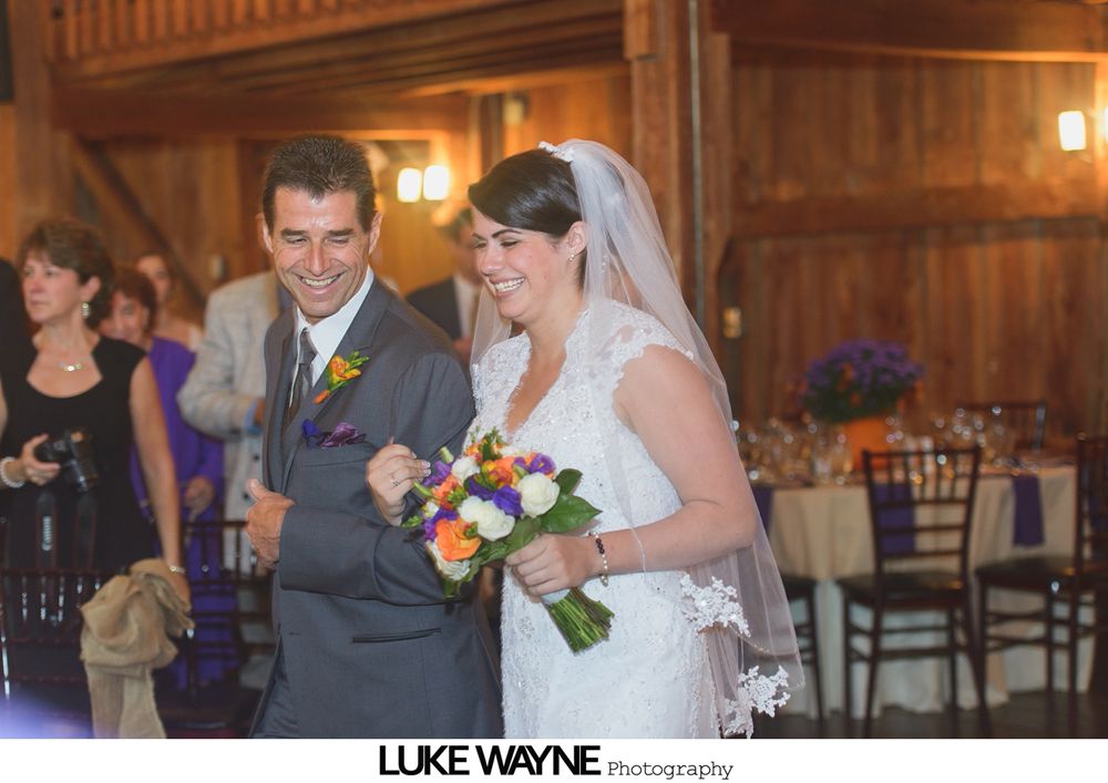 Newlyweds embrace in a pumpkin patch with a blue sky background. The bride wears a white dress, the groom a black suit.