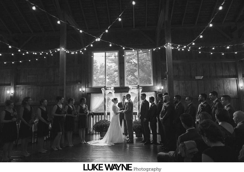 Bride and groom embrace, autumn leaves in background. Groom kisses bride's cheek. Sunlight creates yellow glow.