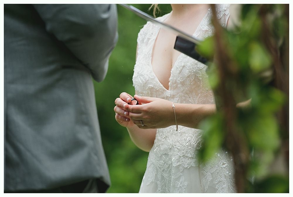 Bride in white lace dress exchanging rings at outdoor wedding ceremony.