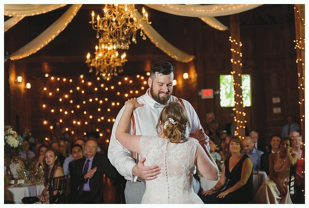 Bride and groom dance at reception; chandelier and string lights illuminate venue.