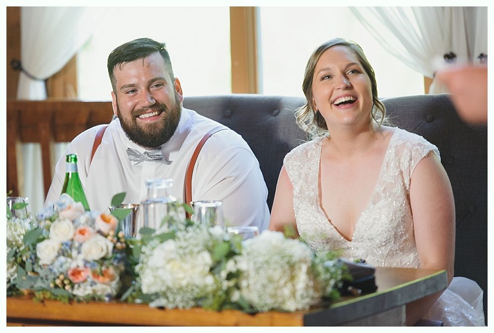 Couple laughing at a wedding reception, seated at a table with floral arrangements.