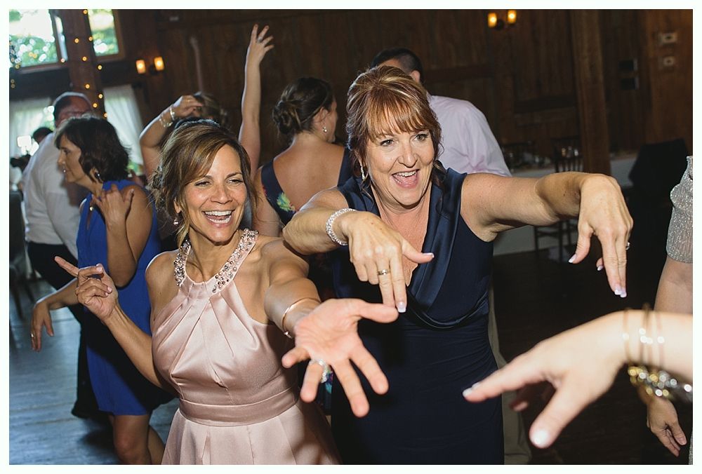 Two women dancing energetically at a wedding reception, smiling with arms outstretched.