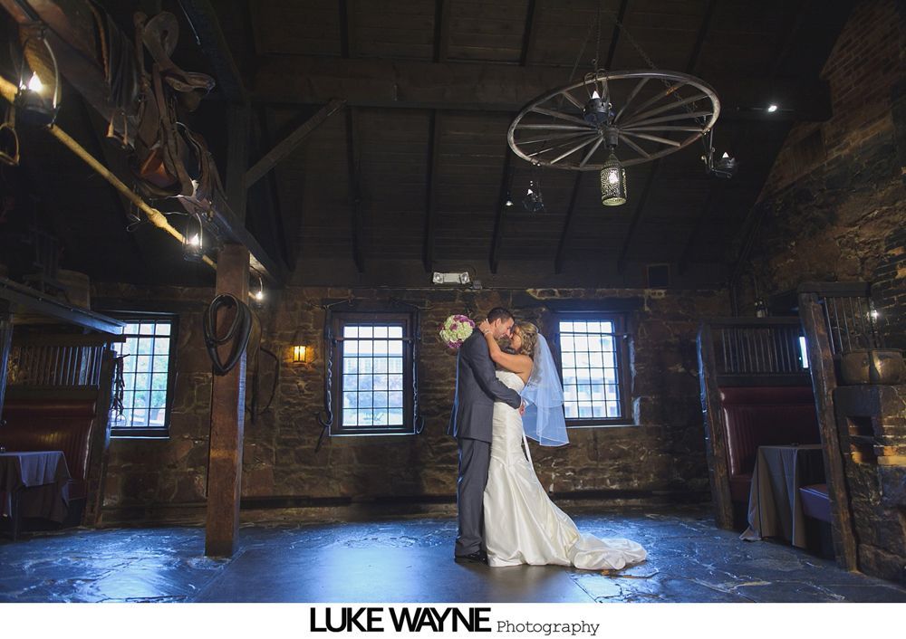 Bride and groom embrace in a rustic barn, lit by soft lighting.