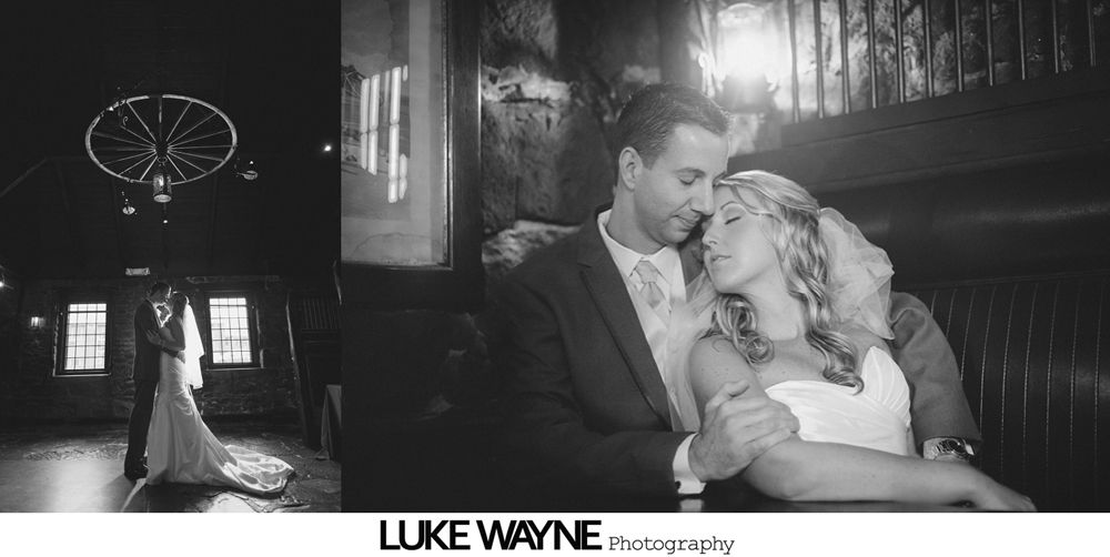 Wedding photo: Couple embracing indoors. Bride in strapless gown, groom in suit. Dark setting.