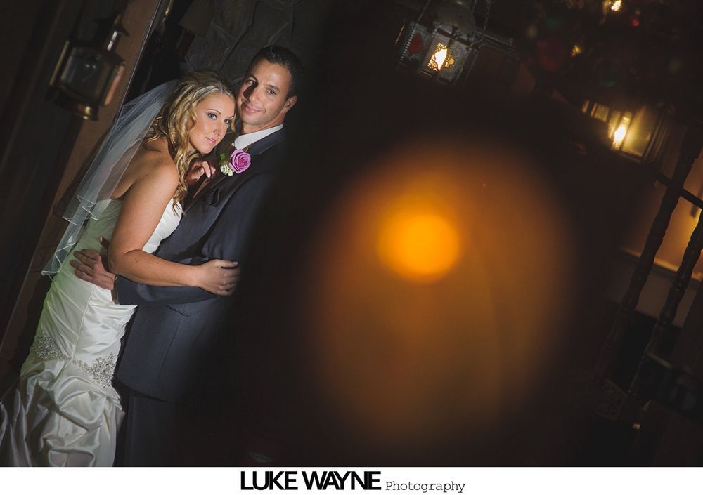 Bride and groom embrace in a dimly lit room, soft lighting accentuates them.