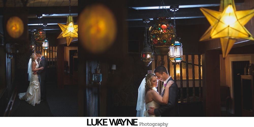 Newlyweds embrace under decorative lights in a warmly lit interior.