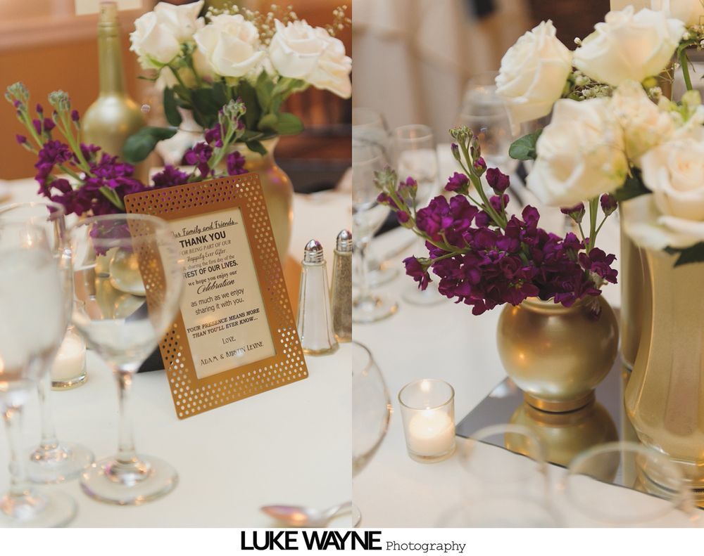 Wedding reception table with white roses, purple flowers, gold vases, and menu card.