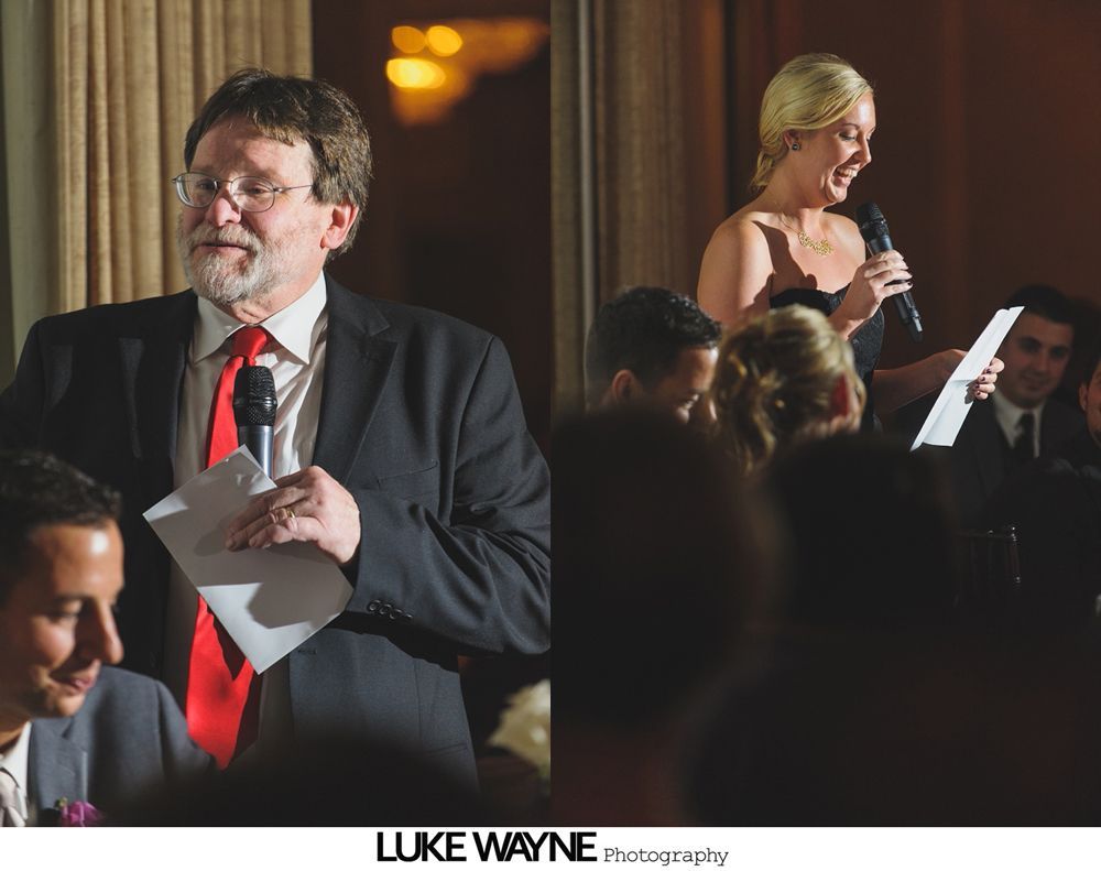 Man in suit with red tie and woman in black dress give toasts at a wedding reception.