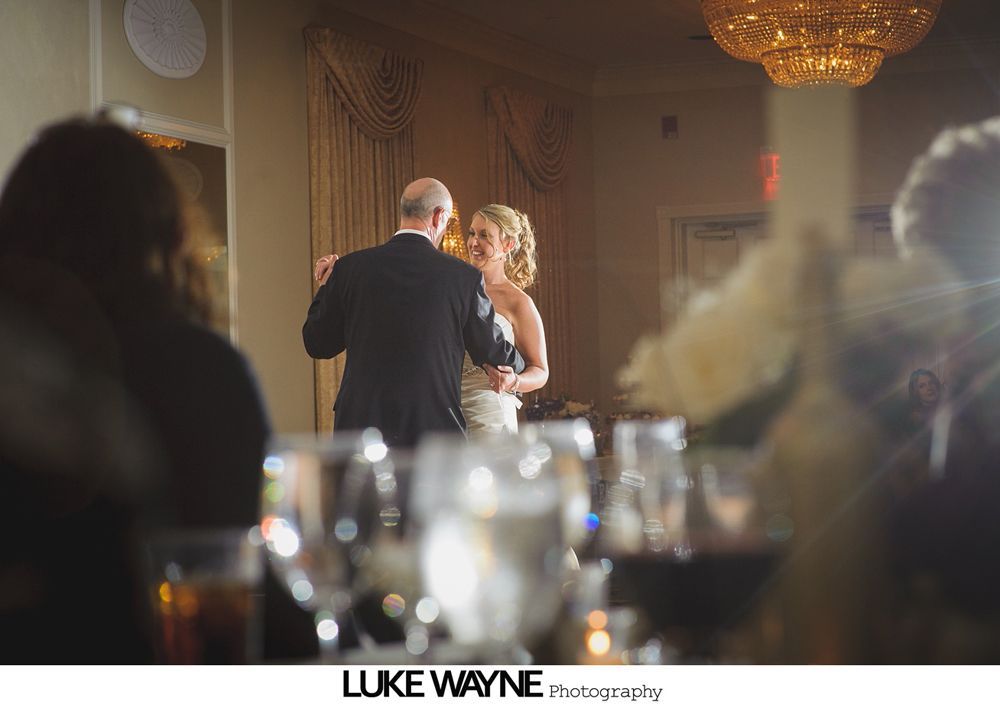 Bride and groom dancing at wedding reception. Sparkling glassware on tables. Warm lighting.