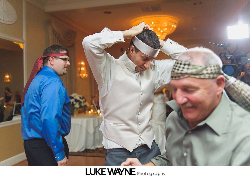 Three men wearing headbands, one putting his on. They are indoors at a wedding reception.