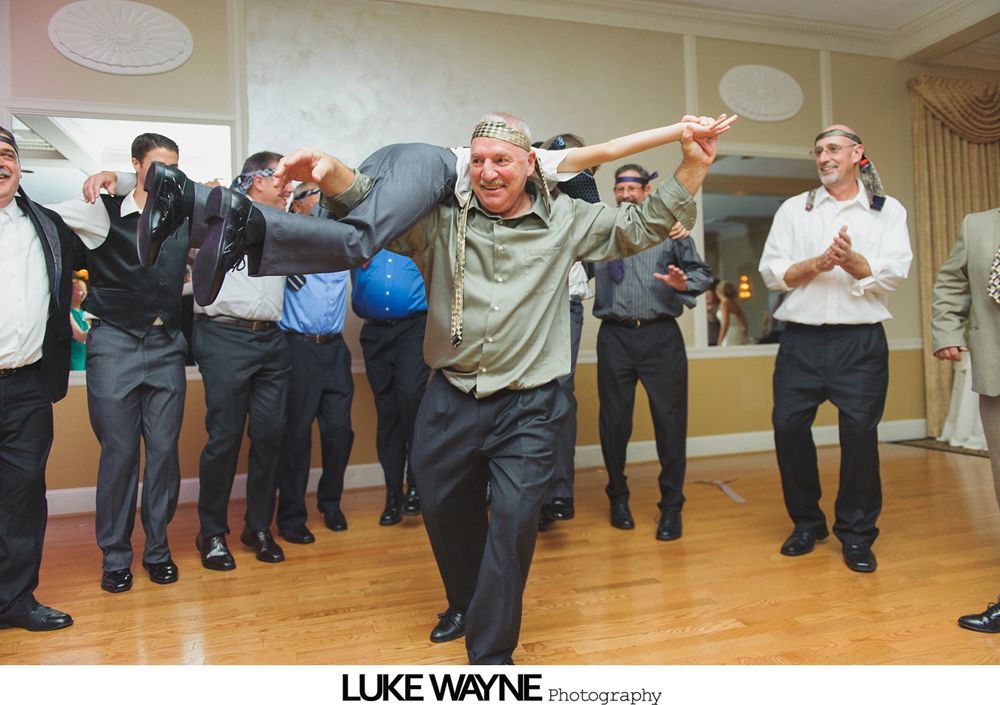 Men dance in a ballroom, one carrying another person, celebratory atmosphere.