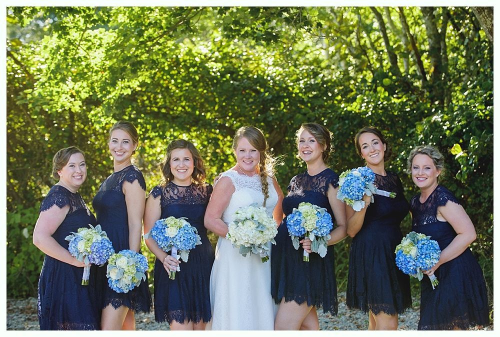 Bride and bridesmaids in navy dresses hold bouquets, posing outdoors.