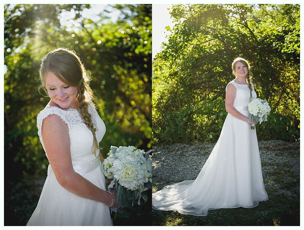 Bride in white gown holding bouquet, posed outdoors. Sunlight streams through trees.