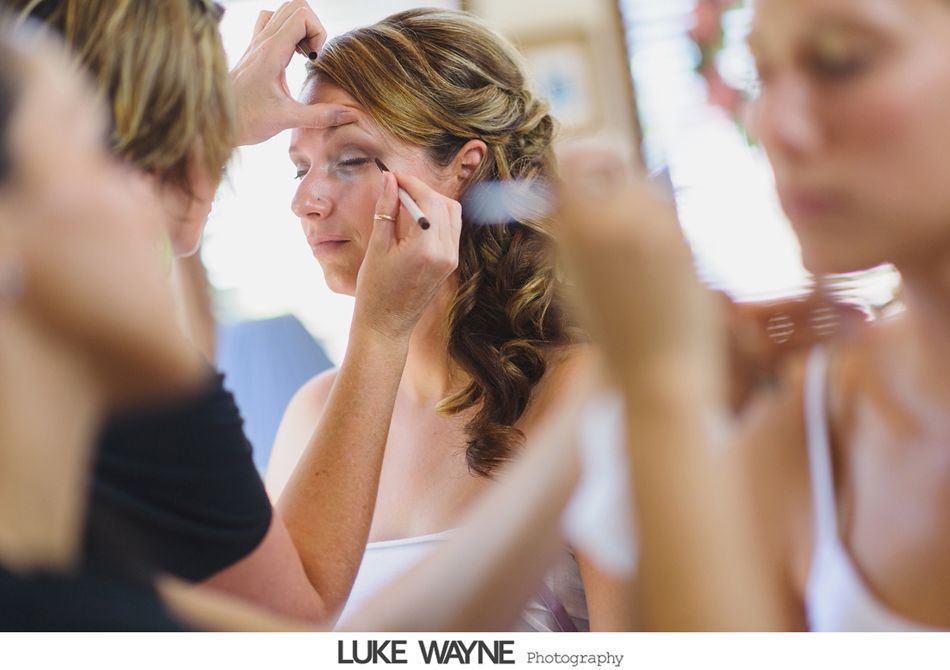 Woman having makeup applied; hair styled. Soft focus, bright room.