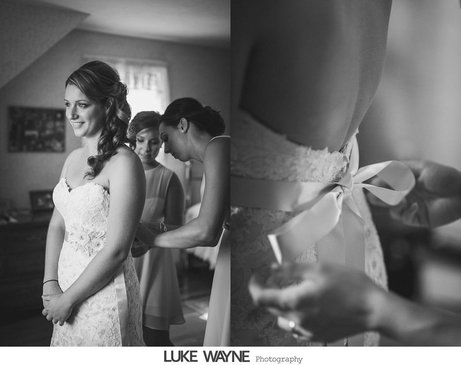 Bride in white lace dress, getting help with the back bow from bridesmaid. Indoor setting. Black and white.