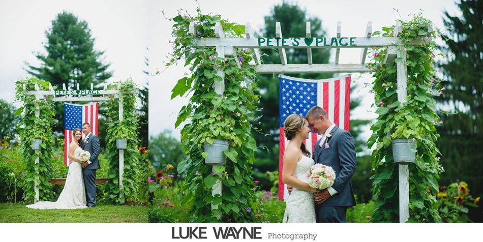 Wedding couple kissing under a floral arch and American flag. 