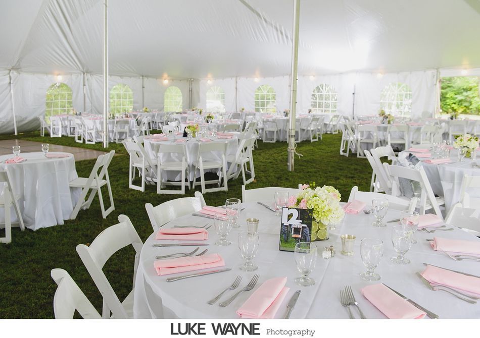 Wedding reception tent: White tables set with pink napkins, white chairs, and floral centerpieces on a grassy lawn.