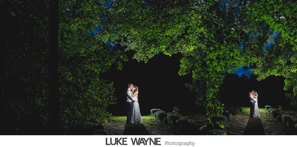 Couple embraces under leafy trees at night, lit by soft light.