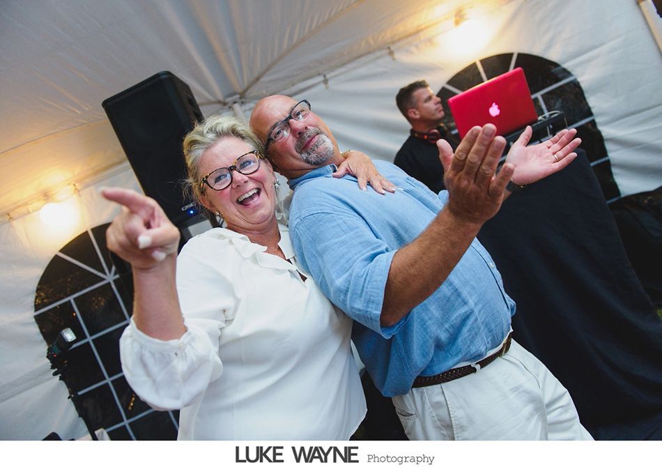 Smiling couple dancing with a red laptop in an outdoor tent. DJ in the background.