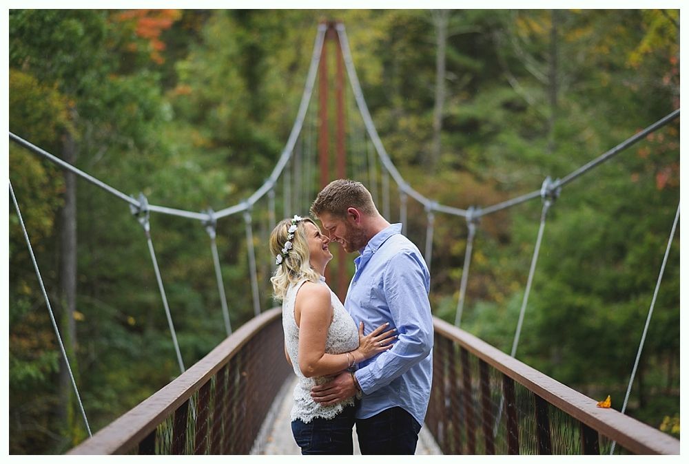 Couple kissing on a suspension bridge, embraced, facing each other. Forest in the background.