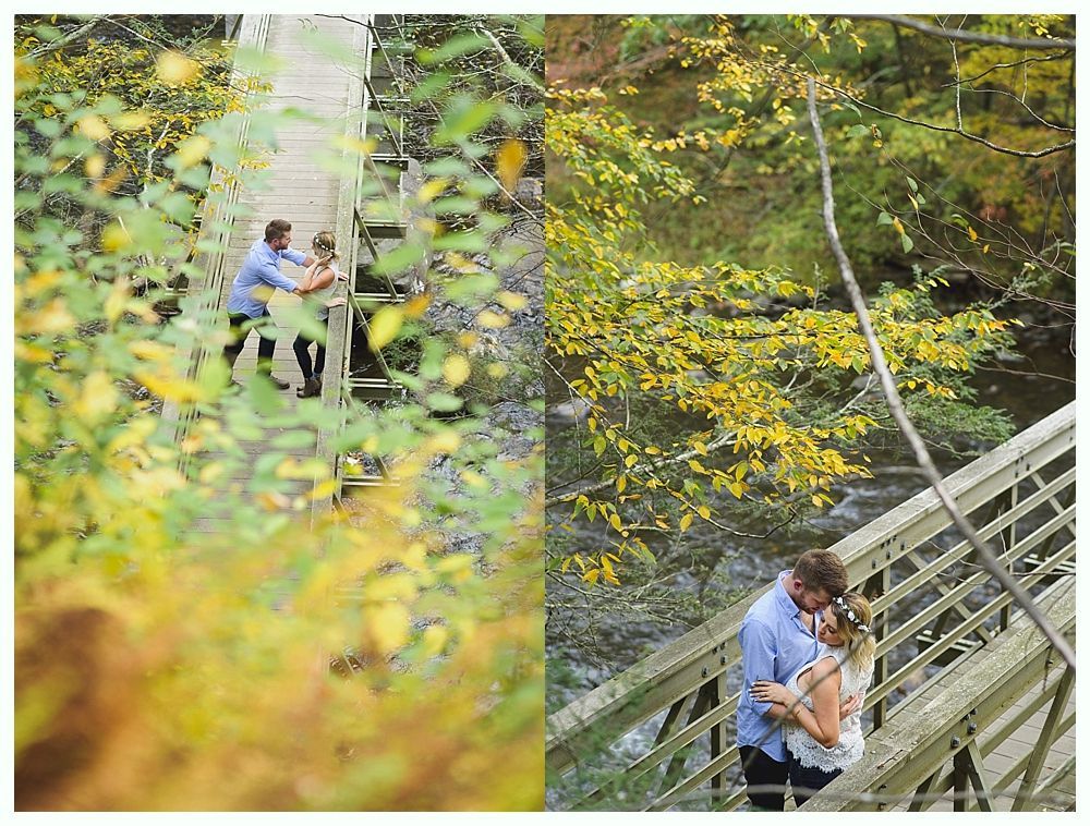 Couple embraces on a wooden bridge over a stream in a forest, surrounded by fall foliage.