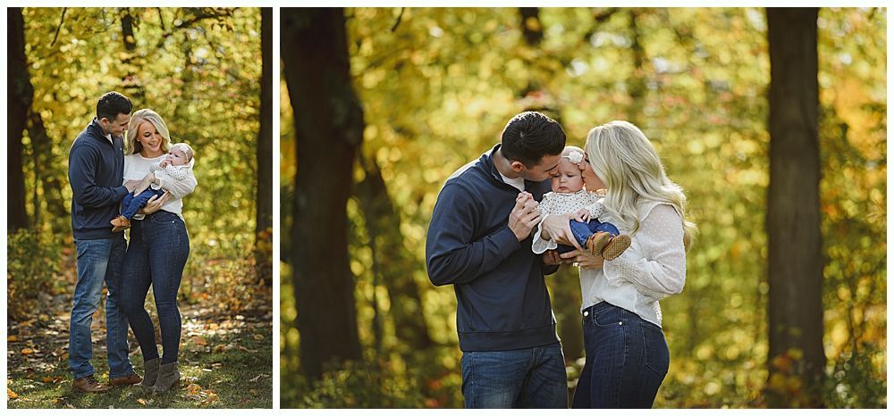 Family of three in a forest; parents kissing a baby. Autumn foliage in background.