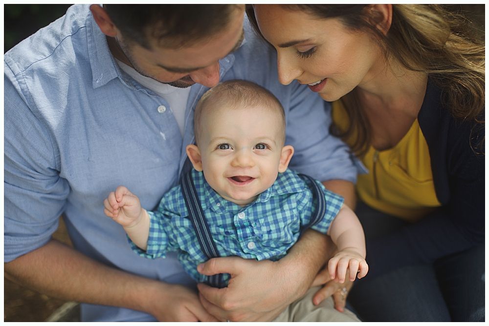 Parents holding and smiling at a happy baby, wearing blue plaid shirt and suspenders.