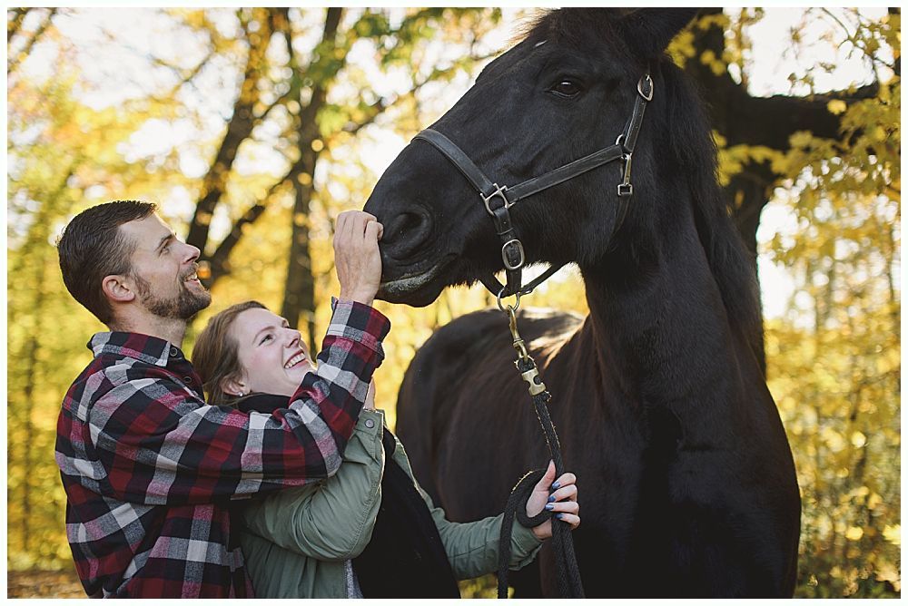Couple petting a black horse in an autumn setting with golden leaves.