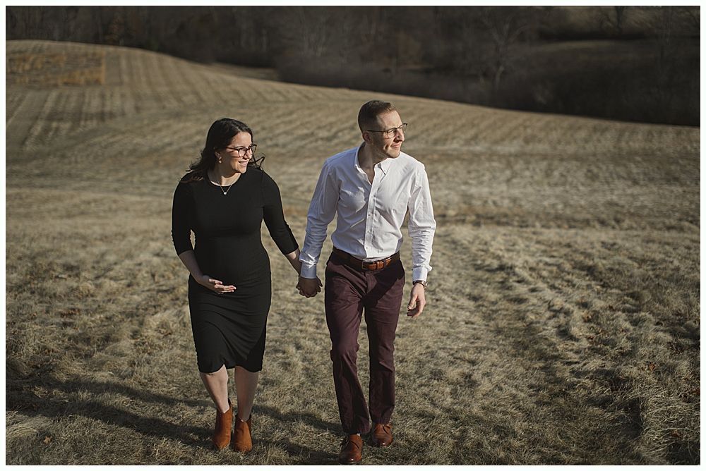 Couple holding hands, walking in field, woman touches pregnant belly.