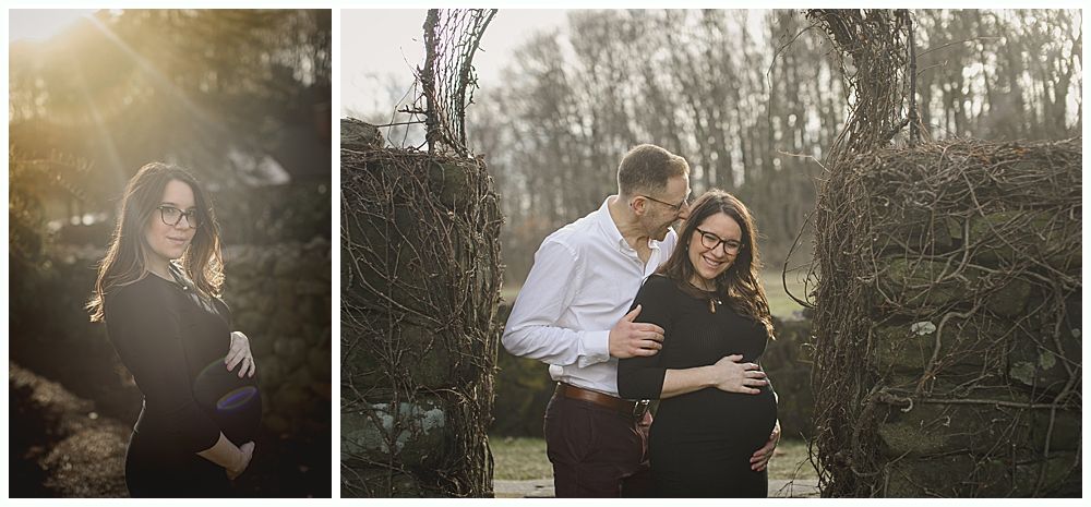 Pregnant woman and man pose for a maternity photo in a garden. The woman is wearing glasses and a black dress.