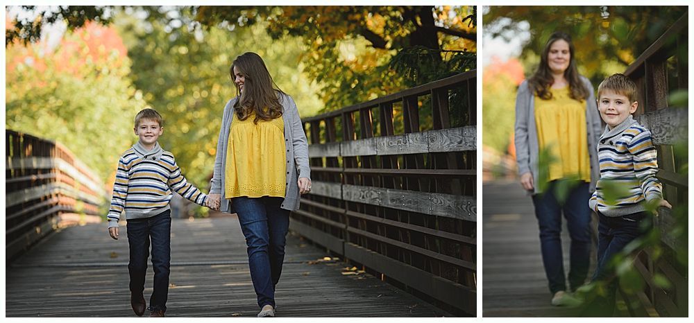 Woman and boy walk hand-in-hand on wooden bridge, fall foliage.
